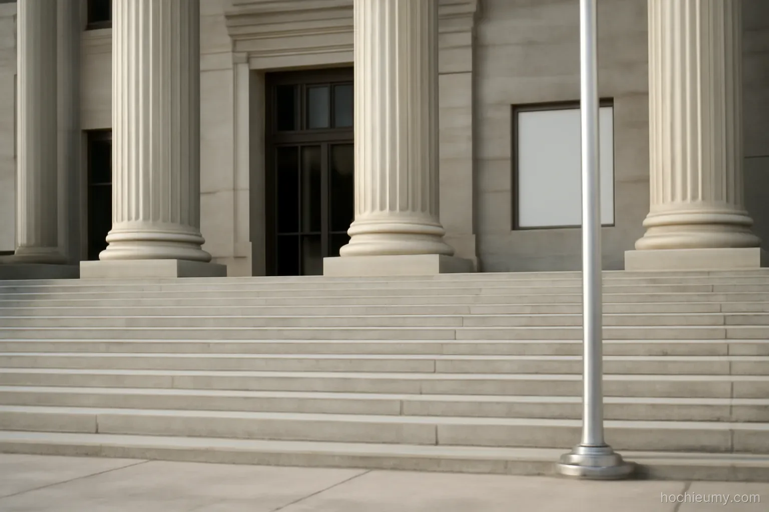 a government building entrance with wide stone steps and a flagpole standing empty beside it